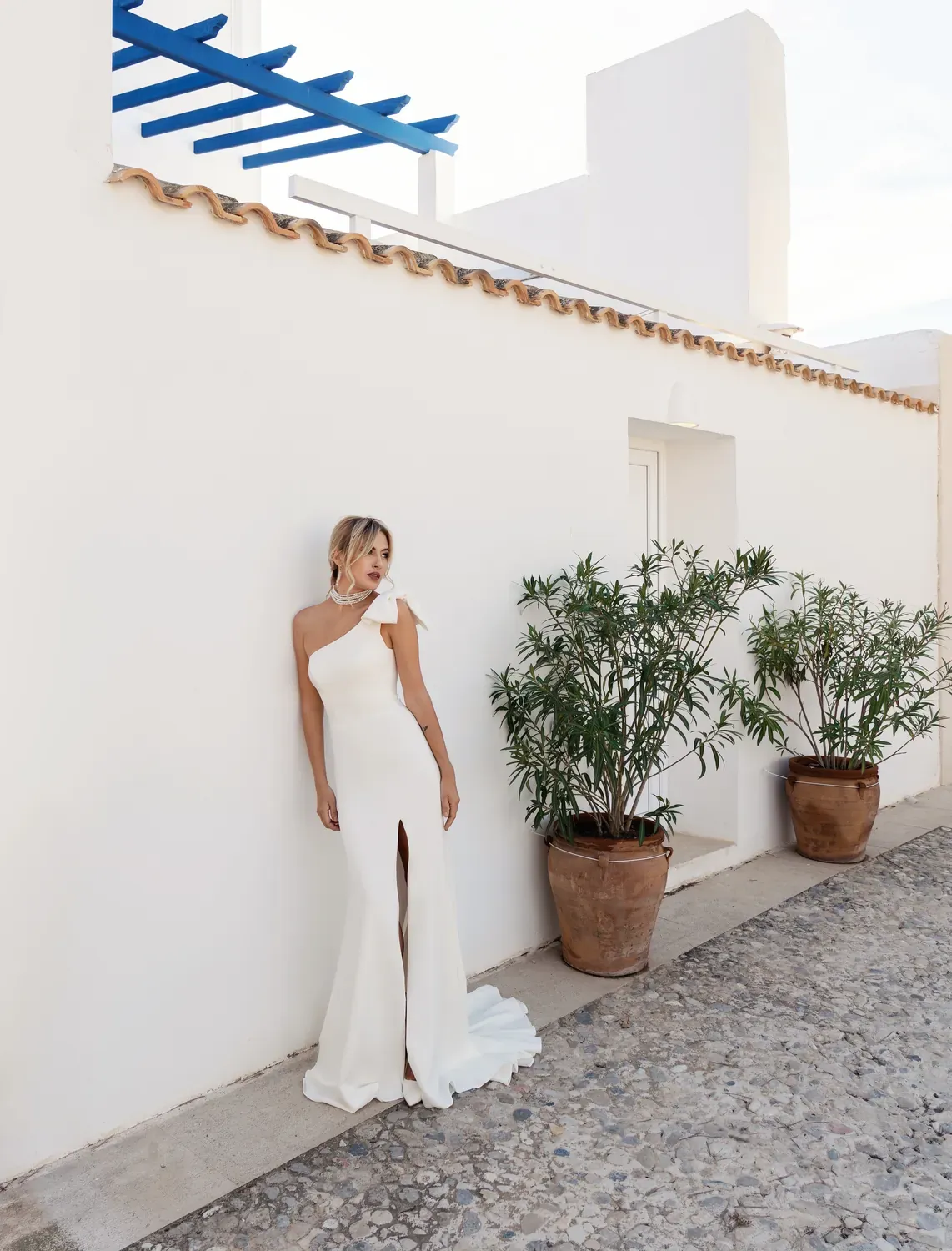 Vestido Alba de un solo hombro con lazo, junto a una pérgola azul