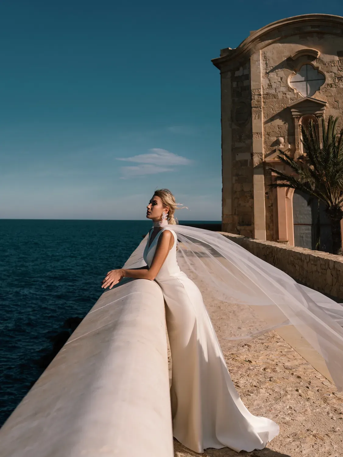Vestido Levante de JJ Bridal con capa de tul volando sobre el mar